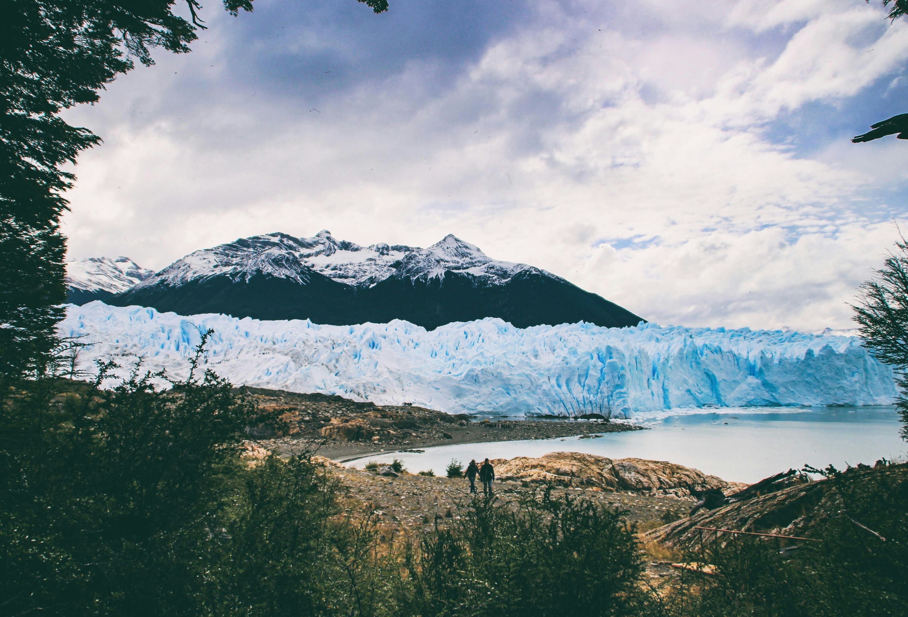 two people hiking towards a large glacier with a mountain in the background